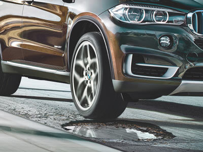 BMW vehicle driving over a pothole in the road